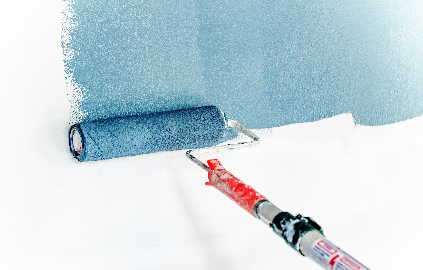 Paint roller applying fresh dusty-blue paint to a white wall